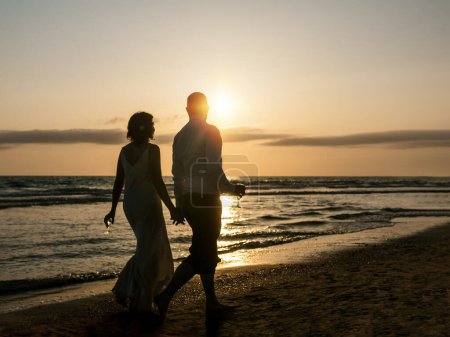 Die Silhouette eines Paares, das Hand in Hand am Strand entlang geht, mit dem Sonnenuntergang im Hintergrund.