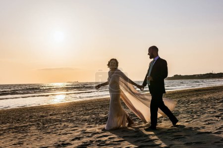 Die Silhouette eines Paares, das Hand in Hand am Strand entlang geht, mit dem Sonnenuntergang im Hintergrund.