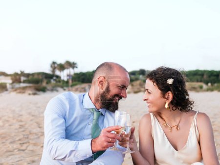 Téléchargez les photos : Couple toasting avec du vin sur une plage sereine pendant l'heure d'or. - en image libre de droit