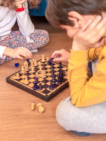 Two children deeply focused on playing chess, sitting on the floor.