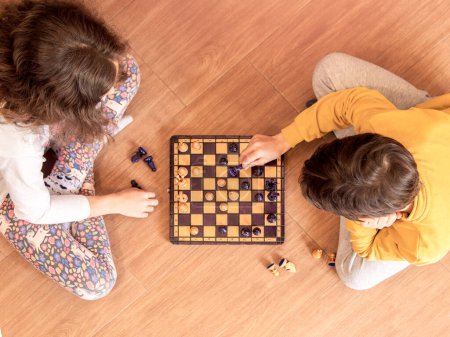 Deux enfants profondément concentrés sur le jeu d'échecs, assis par terre.
