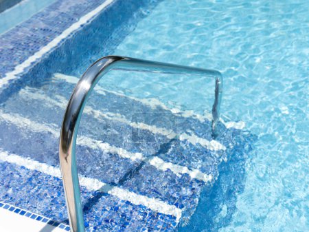 Stainless steel ladder descending into vibrant blue pool water.