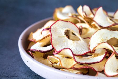Foto de Chips hechos en casa secas de manzana orgánica en rodajas en un primer plano tazón. Concepto de bocadillos saludables - Imagen libre de derechos