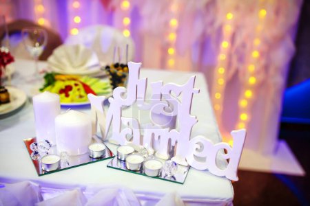 Téléchargez les photos : "Just Married" white wooden letters with candles on holiday table. Wedding decor. Celebrating wedding ceremony concept - en image libre de droit