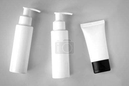 Téléchargez les photos : Bouteilles blanches et tube de produits cosmétiques avec maquette de marque sur fond gris. Soin de la peau et concept beauté - en image libre de droit