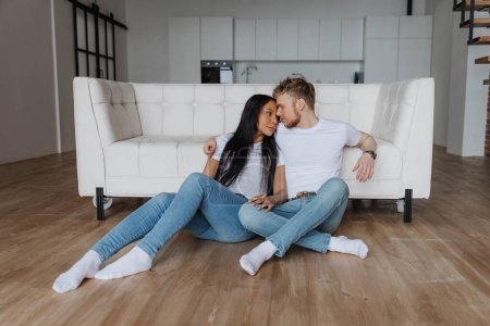 Téléchargez les photos : Jeune couple heureux assis sur le sol à la maison et se regardant - en image libre de droit