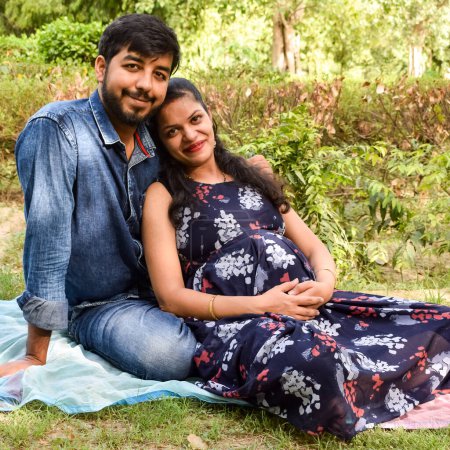 Couple indien posant pour la maternité bébé shoot. Le couple pose dans une pelouse avec de l'herbe verte et la femme faufile sa bosse de bébé dans le jardin Lodhi à New Delhi, en Inde