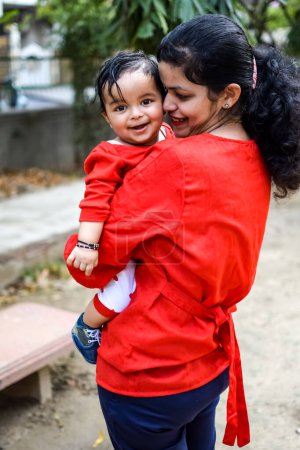 Foto de Madre cariñosa cargando a su bebé en el parque social. Brillante retrato de mamá feliz sosteniendo al niño en sus manos. Madre abrazando a su pequeño hijo de 9 meses. - Imagen libre de derechos