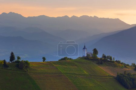 Téléchargez les photos : Eglise Jamnik dans les Alpes slovènes dans une belle matinée lumière différente, avec les Alpes en arrière-plan. - en image libre de droit