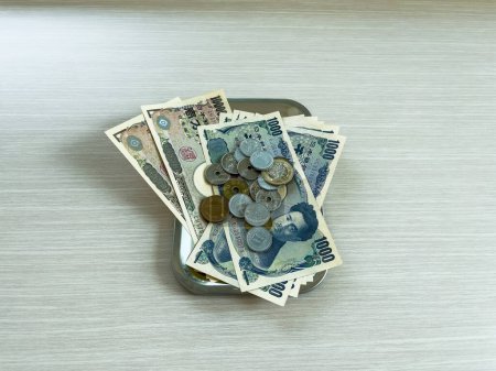 Billetes y monedas de yen de varias denominaciones se colocan en una bandeja de cambio en un piso de madera.