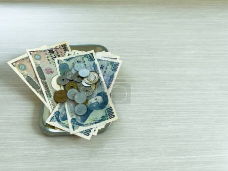 Los billetes y monedas de yen de varias denominaciones se colocan en una bandeja de cambio en un suelo de madera. Copiar espacio fondo