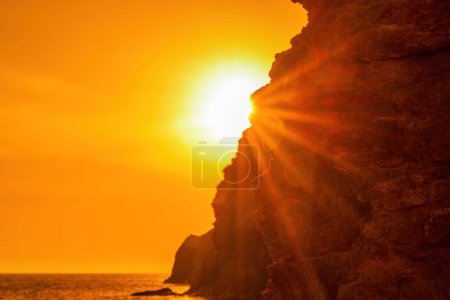 Téléchargez les photos : Femme touriste profitant du coucher de soleil sur le paysage de montagne de la mer. Assis à l'extérieur sur un rocher au-dessus de la mer. Elle porte un jean et une capuche bleue. Mode de vie sain, harmonie et méditation. - en image libre de droit