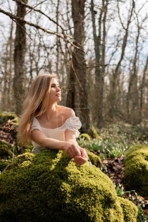 Photo for Snowdrops galanthus blonde. A girl in a white dress sits on a meadow with snowdrops in a spring forest. - Royalty Free Image