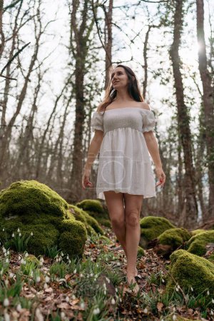 Photo for Snowdrops galanthus woman. She stands in a white dress on a meadow with snowdrops in a spring forest. - Royalty Free Image