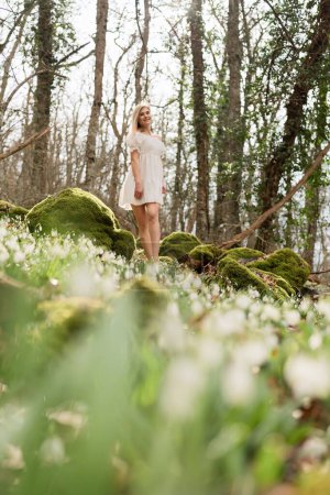 Photo for Snowdrops galanthus blonde. A girl in a white dress stands on a meadow with snowdrops in a spring forest. - Royalty Free Image