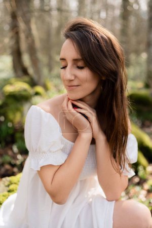 Photo for Portrait of a woman in the forest. She is sitting in a white dress on a meadow with snowdrops in a spring forest. - Royalty Free Image