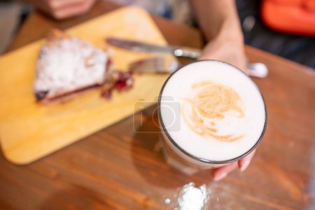 las manos de mujer con café con leche en una mesa de madera en la cafetería.