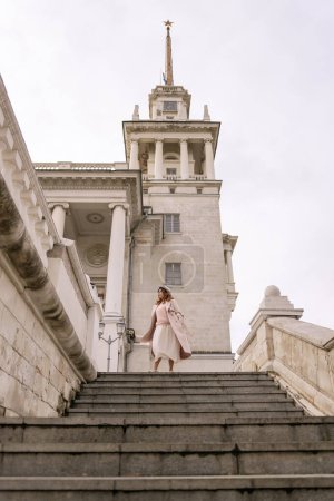 Photo for Woman in elegant coat and hat against an intricate architectural backdrop, harmoniously blending modern fashion with historical allure. The soft daylight adds to its timeless appeal - Royalty Free Image