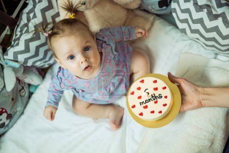 Téléchargez les photos : Bébé fille mignonne célèbre 6ème mois à partir de la naissance. Bonne petite fille obtient gâteau avec une bougie. Fille 6ème mois fête. - en image libre de droit