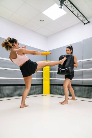 Photo for Vertical image of a Kickboxer doing a front kick during a practice with her colleague in the ring at the gym. - Royalty Free Image