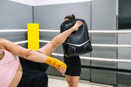 Photo for Unrecognizable female kickboxer giving a high kick in training with his coach in the ring. - Royalty Free Image