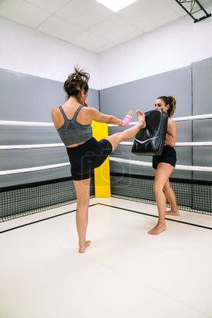 Photo for Vertical image of a confident young female athlete practicing a front kick during a practice with her partner at the gym. - Royalty Free Image