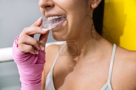 Midsection of a female athlete putting on a mouth guard in boxing training in a ring.