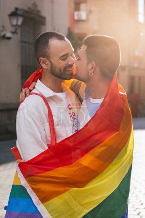 Photo for In a sun-drenched city street at dusk, two gay friends, adorned with vibrant LGBT symbols, share a tender embrace and gaze. - Royalty Free Image