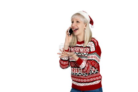 Téléchargez les photos : Joyeux blond dans le chapeau du Père Noël bavarder sur mobile, en chandail de vacances festive. - en image libre de droit