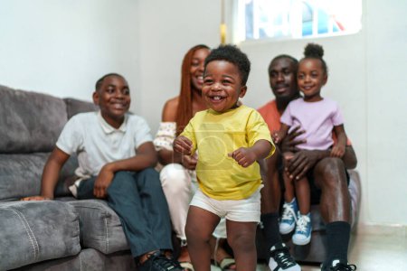 Téléchargez les photos : Heureuse famille africaine avec des enfants joyeux souriant et collant sur le canapé du salon. - en image libre de droit