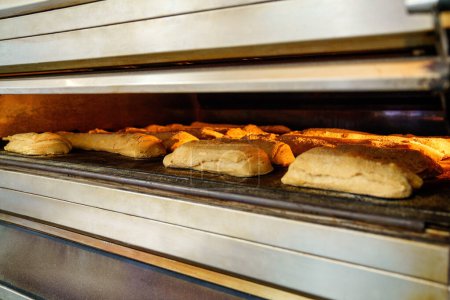 Foto de Panes de pan artesanal horneado a un perfecto marrón dorado en un gran horno industrial, en una panadería. - Imagen libre de derechos