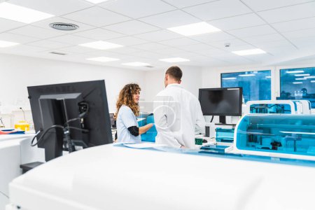 Téléchargez les photos : Deux techniciens de laboratoire conversent au milieu de machines d'analyse de sang dans un environnement de laboratoire hospitalier propre et lumineux. - en image libre de droit