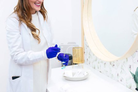 Téléchargez les photos : Médecin heureux méconnaissable en manteau blanc et gants bleus tenant une seringue d'acide hyaluronique dans une clinique esthétique moderne - en image libre de droit