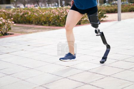 Foto de Enfócate en la pierna protésica deportiva de fibra de carbono de un corredor en movimiento, con pavimento borroso y vegetación en el fondo. - Imagen libre de derechos