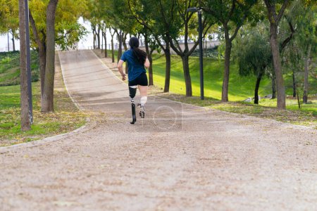 Foto de Vista trasera de un corredor con una pierna protésica deportiva de alta tecnología, acelerando en un sendero del parque rodeado de naturaleza - Imagen libre de derechos