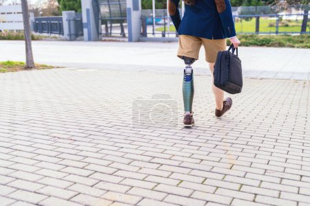 Photo for Unrecognizable businessman with artificial leg briskly walking on a cobblestone walkway, focused on his journey ahead - Royalty Free Image