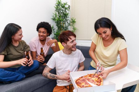 Photo for Friends gather on a couch for a birthday celebration, toasting with beers and sharing delicious pizza in a relaxed apartment space. - Royalty Free Image