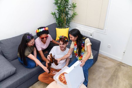 Photo for Cheerful young adults sharing pizzas and beers, enjoying each other's company on a couch during a colorful and casual birthday party. - Royalty Free Image
