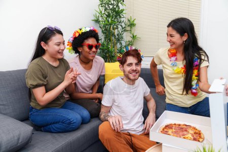 Téléchargez les photos : Groupe de jeunes, divers amis ayant une fête d'anniversaire à la maison. Ils partagent des rires et des pizzas sur le canapé, avec un décor joyeux et des vêtements. - en image libre de droit