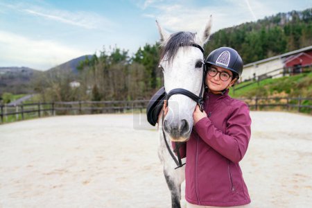 Lächelndes Reitermädchen mit Brille teilt einen zarten Moment mit ihrem gefleckten Schimmel in einer Arena