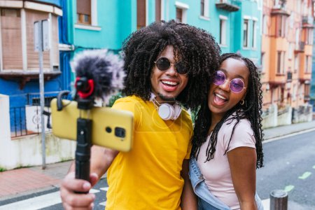 Vibrantes jóvenes influencers latinos transmitiendo en vivo con casas coloridas en el fondo