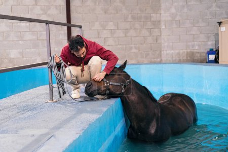 Ein Pferd ruht nach einer Reha mit einem fürsorglichen Trainer in einem Hydrotherapie-Pool.