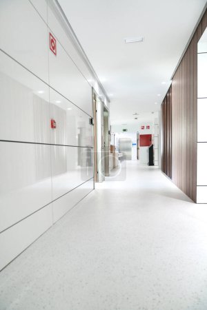 Couloir d'hôpital lumineux et stérile avec signalisation d'urgence visible.