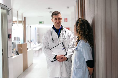 Personal médico alegre comprometido en la conversación en un pasillo de la clínica.