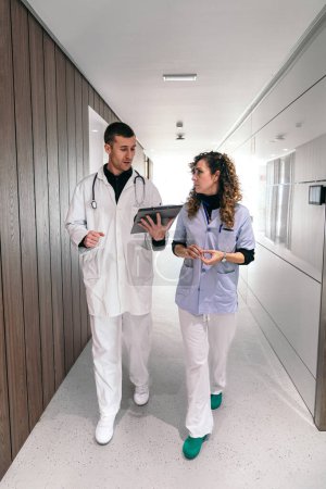 Téléchargez les photos : Médecin et infirmière en conversation profonde en marchant dans une clinique. - en image libre de droit