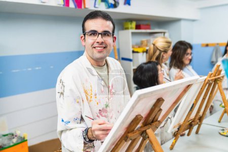 Un homme concentré avec des lunettes peignant dans une classe d'art adaptée aux personnes handicapées."