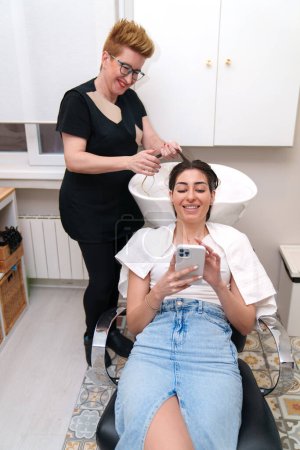 Frau telefoniert während einer Haarbehandlung