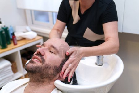 Photo for Man enjoys a gentle scalp wash at a hair clinic. - Royalty Free Image