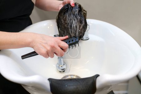 Photo for Stylist's hands rinse a hairpiece at a clinic sink. - Royalty Free Image