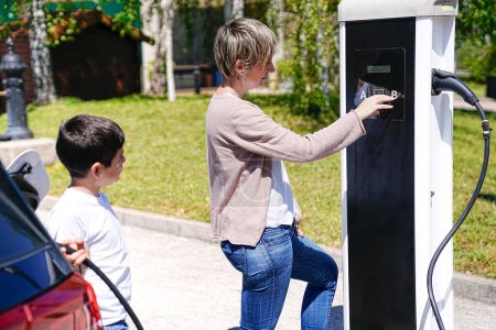 A mother cheerfully instructs her son on EV charging on a radiant day.